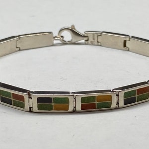 May include: A silver bracelet with a series of rectangular links, each featuring a colourful enamel design of four squares in green, red, yellow, and black.
