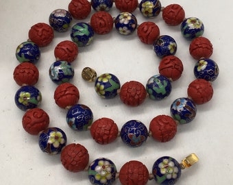 May include: A red and blue beaded necklace with carved and enamel details. The beads are round and feature floral and Chinese character designs. The necklace has a gold clasp.