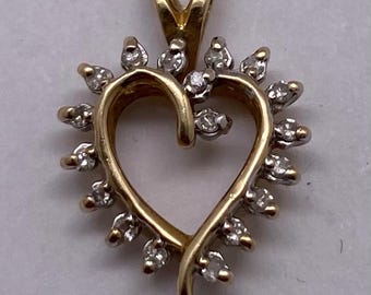 May include: A gold-colored heart-shaped pendant with small, clear gemstones around the edges. The pendant has a loop at the top for a chain. The gemstones are arranged to create a sparkling effect.