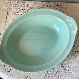 May include: A light blue oval serving dish with a slightly raised rim and two handles. The dish has a glossy finish and a crackled texture. The dish is likely made of ceramic or porcelain.