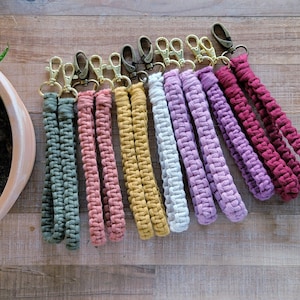 May include: A set of ten colorful braided keychains with gold metal clasps. The keychains are made of cotton cord and come in a variety of colors, including green, pink, red, purple, and white.