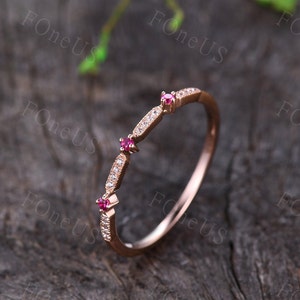 May include: A delicate rose gold band ring with three small ruby stones and a row of pave diamonds.