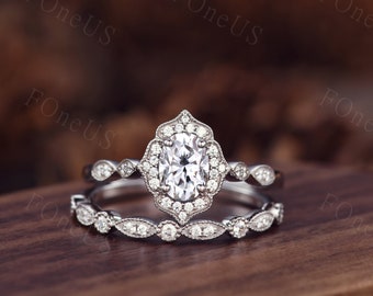 May include: A silver engagement ring set with a large oval-shaped center stone surrounded by smaller diamonds. The ring is set in a delicate filigree design. The band is also set with smaller diamonds.