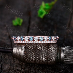 May include: A rose gold band ring with a double row of sparkling stones. The top row features alternating blue and white round stones, while the bottom row is a continuous band of white round stones.