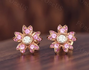May include: A pair of gold flower-shaped earrings with pink gemstones and a clear center stone.