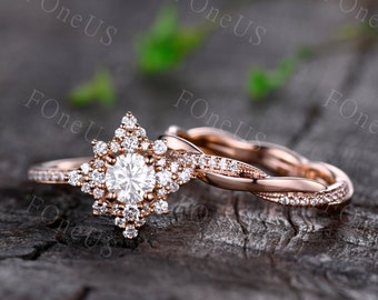 Può includere: Un set di anelli di fidanzamento in oro rosa con una pietra centrale rotonda e un alone di pietre più piccole. La fascia è di design intrecciato con pietre pavé.