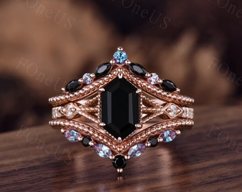May include: A rose gold engagement ring set with a black octagon-shaped center stone and smaller black and blue stones. The ring has a delicate, intricate design.