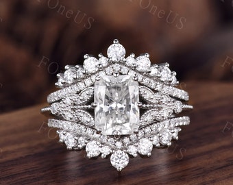 May include: A silver engagement ring with a large, square-cut diamond surrounded by smaller diamonds. The ring has a delicate, intricate design with multiple bands.