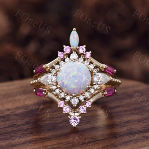 May include: A gold ring with a large white opal gemstone surrounded by smaller clear and pink gemstones. The ring has a delicate, intricate design.