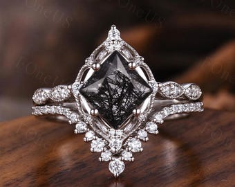May include: A silver-toned ring featuring a kite-shaped black rutilated quartz center stone, surrounded by a decorative filigree setting and small clear accent stones along the band and a V-shaped guard, with the text FOneUS visible.