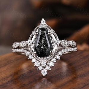 May include: A silver engagement ring set featuring a large, black gemstone with a unique, geometric cut. The ring is surrounded by smaller, clear gemstones and intricate filigree detailing. The set includes a matching band.