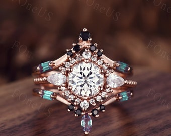 May include: A three-piece rose gold ring set. The engagement ring features a large, round, white center stone surrounded by smaller white stones. The set includes a band with teal and white stones and a crown-shaped band with black stones.