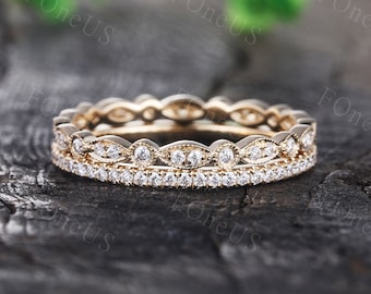 May include: Two delicate gold wedding bands with a vintage design. The top band features a row of small round diamonds set in a scalloped pattern. The bottom band has a row of smaller diamonds set in a straight line.