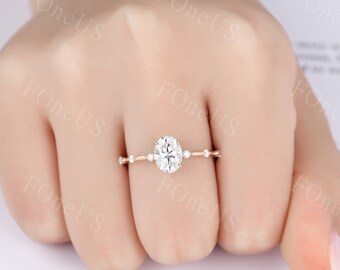 May include: A rose gold engagement ring with an oval-shaped center stone and smaller accent stones. The ring is on a finger.