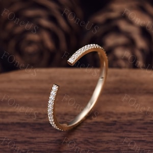 May include: A gold ring with a row of small clear stones set around the band. The ring is open on one side, creating a unique and modern design.