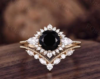 May include: A gold ring set with a black gemstone surrounded by smaller white gemstones. The ring has a delicate, v-shaped band with pear-shaped white gemstones.