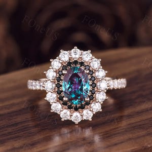 Pode incluir: Anel de ouro rosa com uma gema oval que muda de cor, rodeada por pedras brancas e pretas. A banda é cravejada com pedras brancas menores. Uma joia marcante, perfeita para ocasiões especiais.