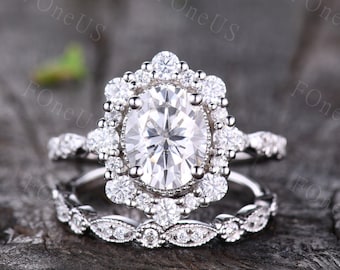 May include: A silver engagement ring set with a large oval-shaped center stone surrounded by smaller stones. The band is decorated with smaller stones and has a delicate floral design.