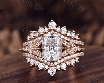 May include: A rose gold engagement ring set with a large square-shaped center stone surrounded by smaller diamonds. The ring has a delicate, intricate design with a floral motif.