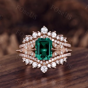 May include: A rose gold engagement ring with a large emerald cut green gemstone surrounded by smaller diamonds. The ring is set in a delicate floral design.