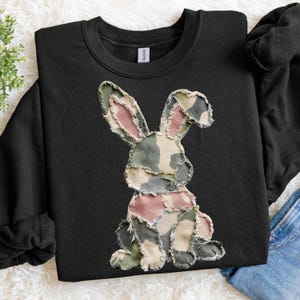 May include: Black crew neck sweatshirt with a patchwork bunny design. The bunny is made of camouflage fabric in green, pink, and beige. A casual, comfortable style.