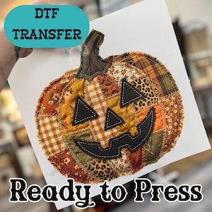 May include: A DTF transfer sheet featuring a patchwork pumpkin design with various autumn-themed fabric patterns including plaid, floral, and leopard print. The pumpkin has black felt-like eyes and a mouth, with visible zigzag stitching.
