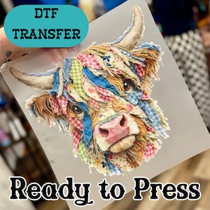 May include: DTF transfer featuring a colorful Highland cow design. The cow's head is adorned with fabric patches in various patterns and colors, including pink, blue, and green. The text "Ready to Press" is displayed below the image.