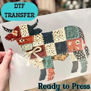 May include: DTF transfer featuring a patchwork cow design. The cow is composed of various fabric patterns in shades of red, blue, green, and cream. The text "DTF TRANSFER" and "Ready to Press" are displayed on the image.