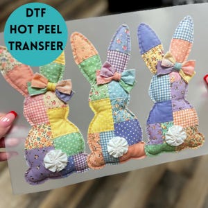 May include: Three colorful bunny-shaped DTF (Direct to Film) hot peel transfers. Each bunny is made of patchwork fabric in various colors and patterns, with a bow and a white flower-like detail. The transfers are on a clear backing.