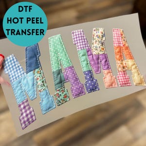 May include: DTF Hot Peel Transfer featuring the word "MAMA" in a patchwork design. Each letter is composed of various fabric patterns, including gingham, floral, and polka dots, in shades of blue, green, purple, and orange.