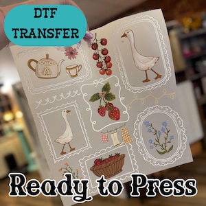 May include: A DTF transfer sheet with various illustrations, including a teapot, teacup, goose, strawberries, and tomatoes, all within decorative frames. The text "DTF TRANSFER" and "Ready to Press" are also visible.