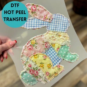 May include: A colorful DTF hot peel transfer featuring a patchwork bunny design. The bunny is composed of various fabric patterns, including floral prints, gingham, and polka dots, with lace accents. The text "DTF HOT PEEL TRANSFER" is in a teal circle.