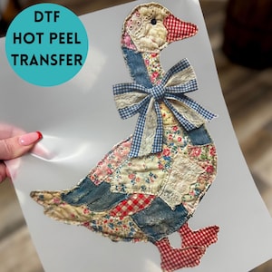 May include: DTF Hot Peel Transfer featuring a patchwork goose design. The goose has a red and white checkered beak and feet, a blue gingham bow, and a body made of floral and denim patches. The text "DTF HOT PEEL TRANSFER" is in a teal circle.
