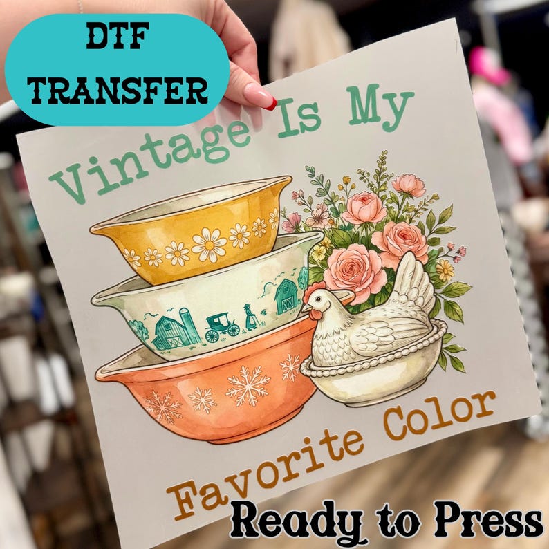 May include: A DTF transfer sheet featuring a stack of three mixing bowls in yellow, cream, and orange, with a white hen figurine, pink roses, and green leaves. The text reads: Vintage Is My Favorite Color Ready to Press.