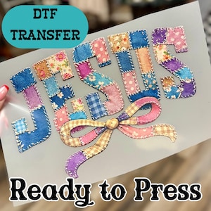 May include: DTF transfer with the word "JESUS" in a patchwork design. The letters are composed of various fabric patterns, including floral and gingham. A large bow with a button center is at the bottom. The text "Ready to Press" is at the bottom.