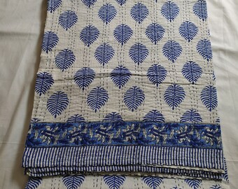 Könnte beinhalten: Eine gefaltete weiß-blaue Steppdecke mit einem Blättermuster. Die Steppdecke hat ein sich wiederholendes Muster aus blauen Blättern auf weißem Hintergrund mit einem blauen Rand. Die Steppdecke besteht aus einem weichen Material und ist ordentlich gefaltet.
