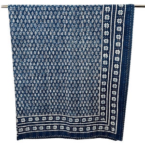 May include: A blue and white kantha quilt with a floral pattern and a border of stars. The quilt is hanging on a rod.