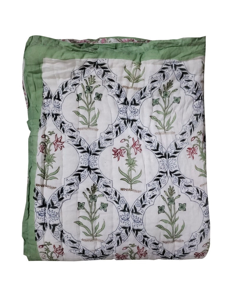 Puede incluir: Una colcha de algod&oacute;n blanco con un borde verde y un patr&oacute;n floral en blanco y negro. La colcha est&aacute; acolchada en forma de diamante.