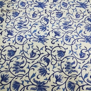 May include: A fabric with a repeating pattern of blue floral designs and swirling vines on a cream background. The flowers are stylized and detailed, creating a visually appealing textile.
