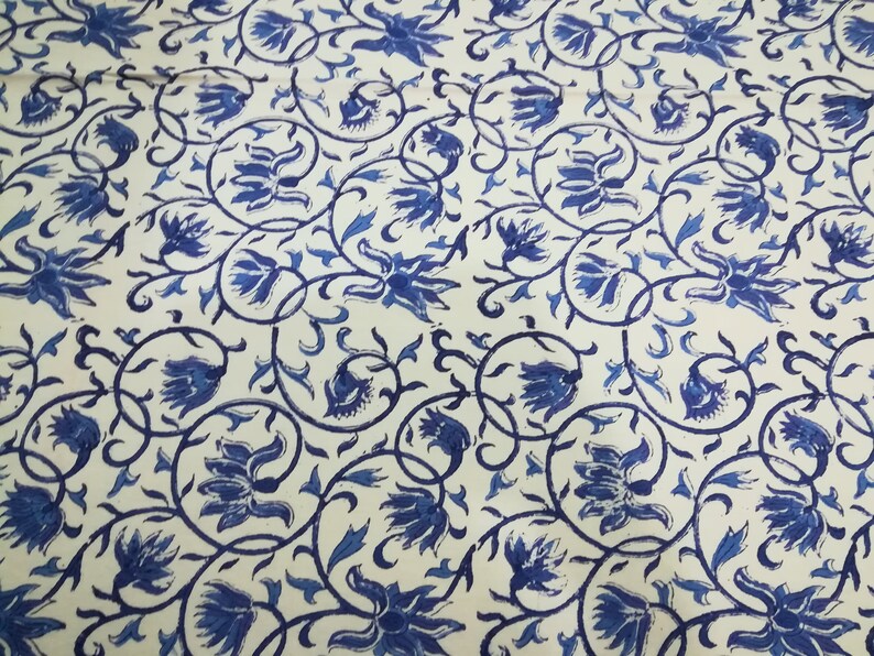 May include: A fabric with a repeating pattern of blue floral designs and swirling vines on a cream background. The flowers are stylized and detailed, creating a visually appealing textile.