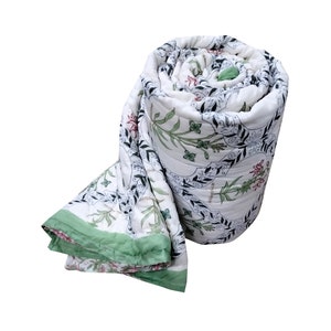 Puede incluir: Una colcha de algod&oacute;n blanco con estampado floral verde y negro. La colcha est&aacute; enrollada y tiene un borde verde.