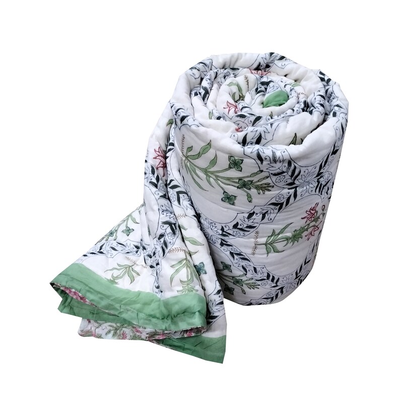 Puede incluir: Una colcha de algod&oacute;n blanco con estampado floral verde y negro. La colcha est&aacute; enrollada y tiene un borde verde.