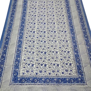 May include: A large, rectangular blue and white patterned textile. The central field features a dense floral design in blue against a white background. A blue border with floral and striped patterns frames the central design. The textile is likely a tablecloth or bedspread.