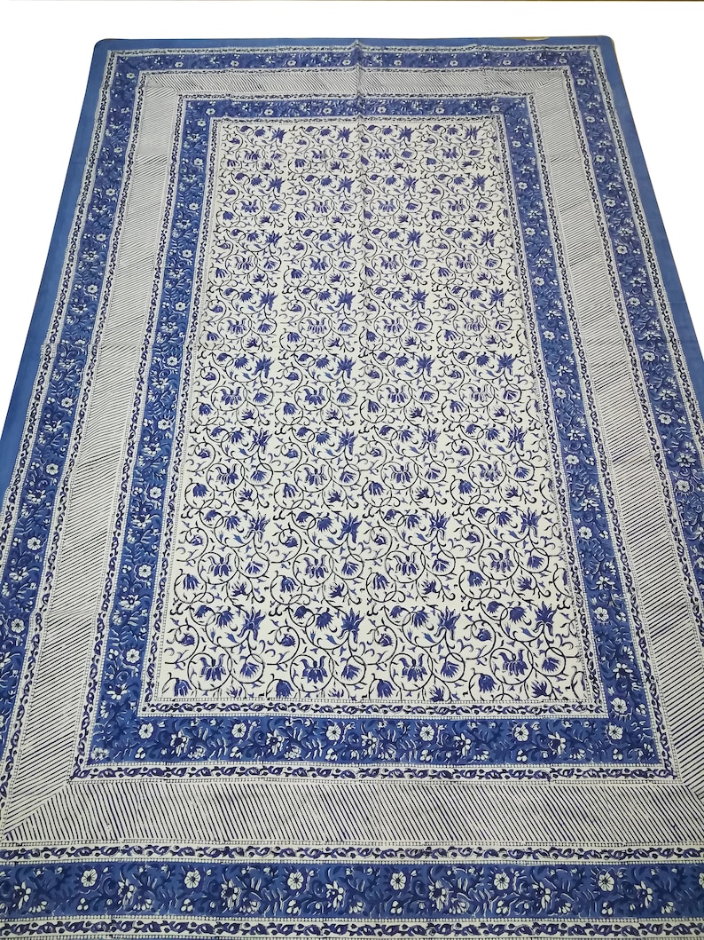 May include: A large, rectangular blue and white patterned textile. The central field features a dense floral design in blue against a white background. A blue border with floral and striped patterns frames the central design. The textile is likely a tablecloth or bedspread.
