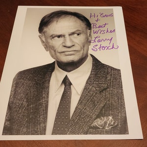 May include: A black and white photo of a man wearing a suit and tie. He is looking at the camera with a serious expression. The photo is signed "Hi Gang + Best Wishes Larry Storch".