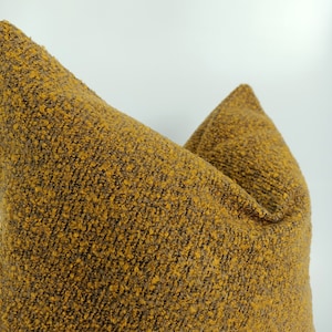 May include: A close-up of a mustard yellow throw pillow with a textured fabric. The pillow is made of a soft, fuzzy material.