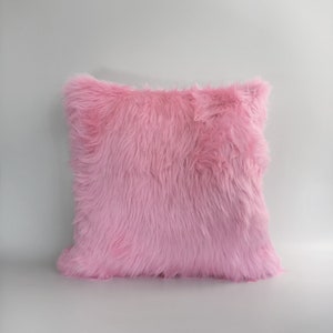 Puede incluir: Una almohada suave de piel sint&eacute;tica rosa. La almohada es de forma cuadrada y tiene una textura esponjosa.