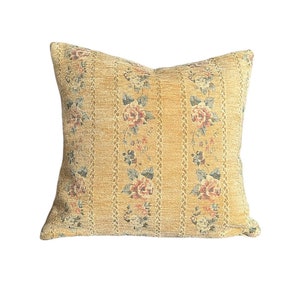 Pode incluir: Uma almofada quadrada com um padrão floral. A almofada é feita de um tecido texturizado e tem um fundo amarelo com flores rosa e azuis.