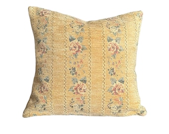 Puede incluir: Una almohada cuadrada con un patrón floral. La almohada está hecha de una tela texturizada y tiene un fondo amarillo con flores rosas y azules.