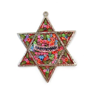 Op de afbeelding: Een zilveren Davidster met een rode achtergrond en een kleurrijk bloemenontwerp. De Davidster heeft de Hebreeuwse woorden "Shalom" op een banner in het midden.
